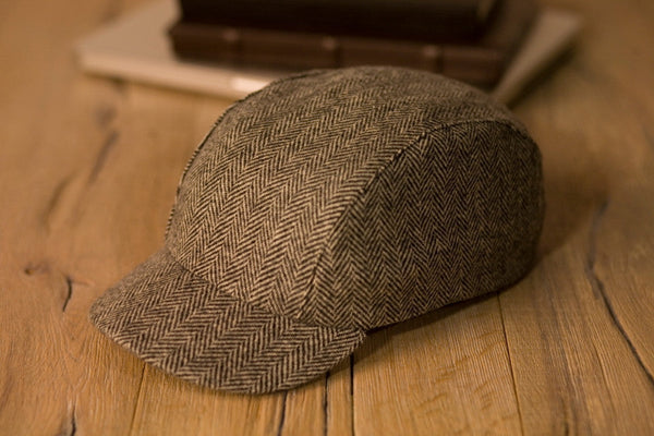 Velo/City Cap - Wool Herringbone #01 3-panel cap lying on a table next to some books.