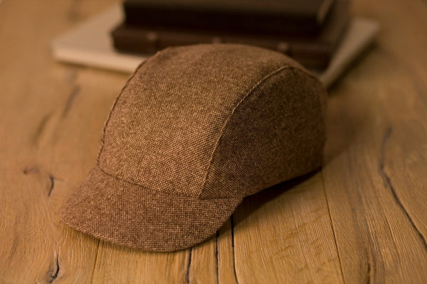 Velo/City Cap - Brown Tweed Wool lying on a table next to some books.