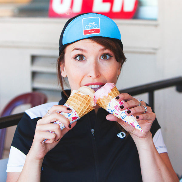 Woman eating two ice cream cones at once, wearing the People for Bikes cap.