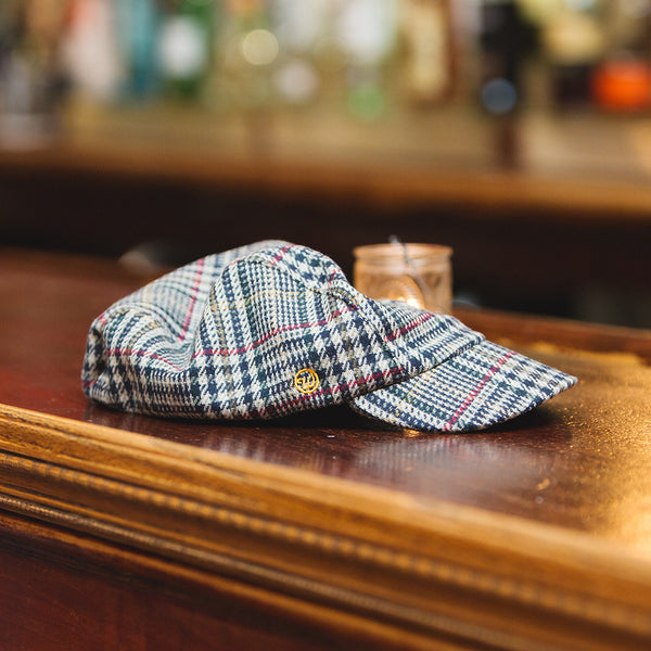The velo/city plaid wool cap lying on a bar-top next to a candle.