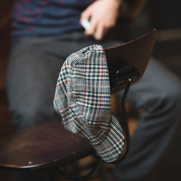 The velo/city plaid wool cap hanging off the back of a chair.