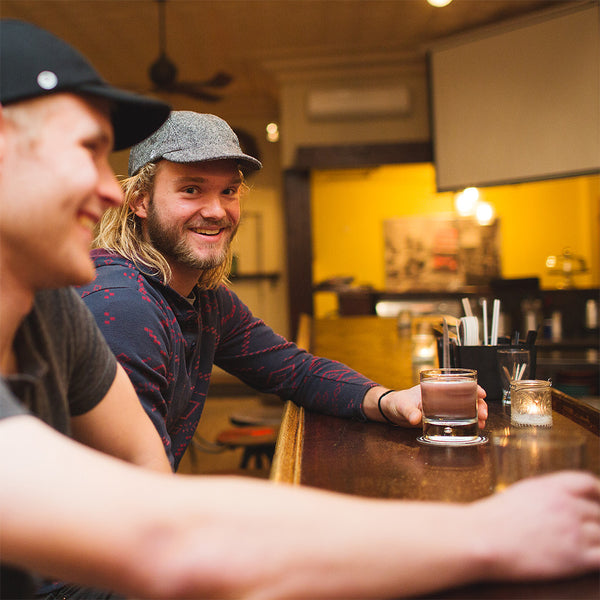 Two men sitting at a bar wearing the black wool and black tweed wool velo/city caps.