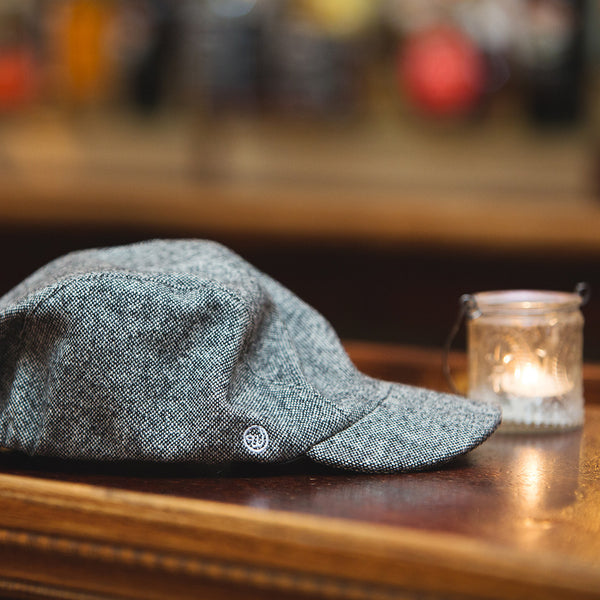 The velo/city black tweed wool cap lying on a bar top next to a candle.