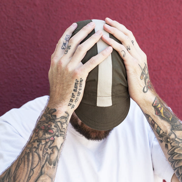 Man wearing woodland cap looking down with hands on head.