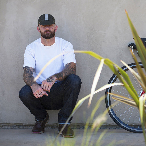 Crouched man wearing woodland cap next to bike.