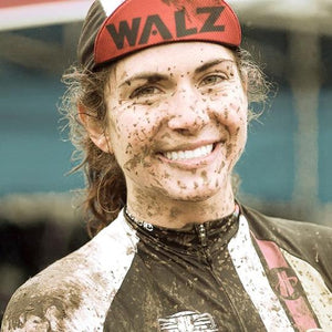 Woman with mud splattered on her face, wearing a walz cap with the brim flipped up.