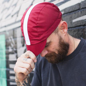 Bearded man tipping his red cotton 3-panel stripe cap.
