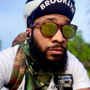Bearded man wearing sunglasses and flipped up Brooklyn cap.
