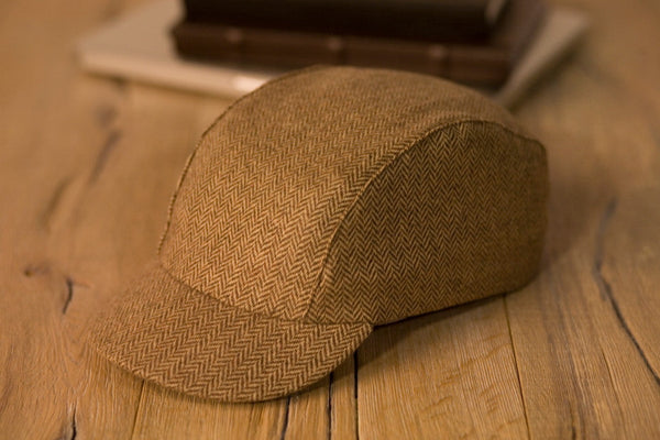 Velo/City Cap - Wool Herringbone #02 3-panel cap lying on a table next to some books.