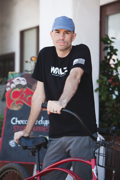 Man posing behind a cruiser bike, wearing the Cool River Cotton Velo/City Cap.