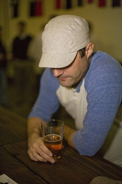 Man drinking a beer at a bar while wearing the speckled hemp velo/city cap.