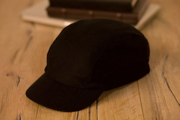 The velo/city black wool cap lying on a table top next to some books.