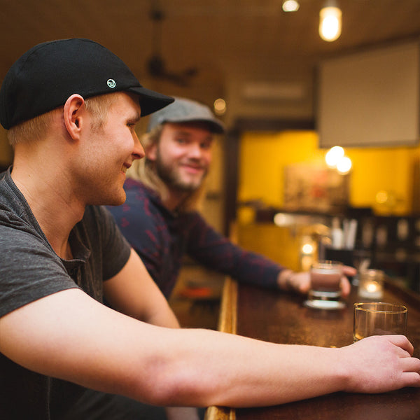 Two men sitting at a bar wearing the black wool and black tweed wool velo/city caps.