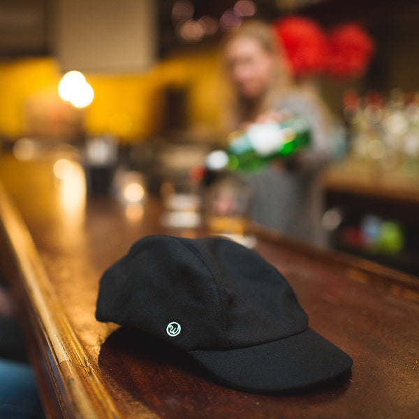 The velo/city black wool cap lying on a bar top.