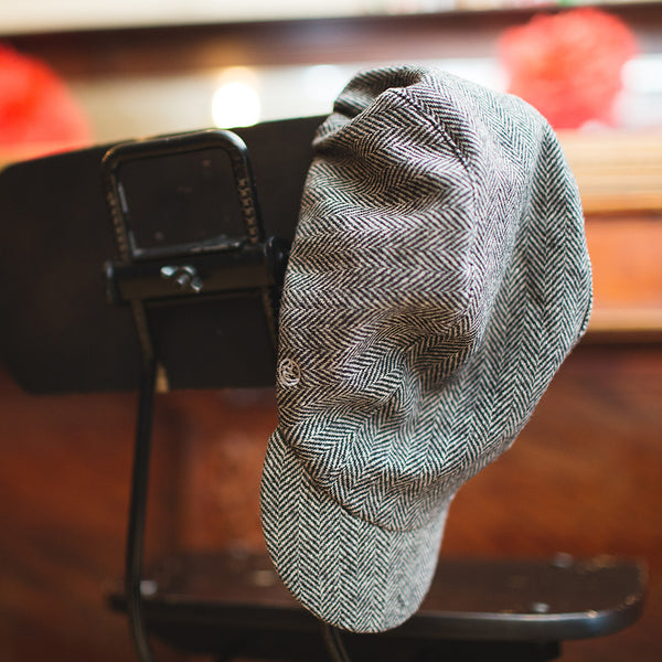 Velo/City Cap - Wool Herringbone #01 3-panel cap hanging off the back of a chair.