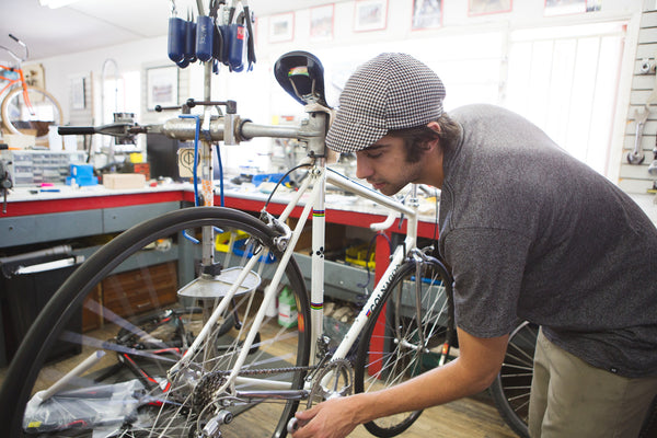 Bike mechanic working on a white bike wearing the black houndstooth wool 4-panel cap.